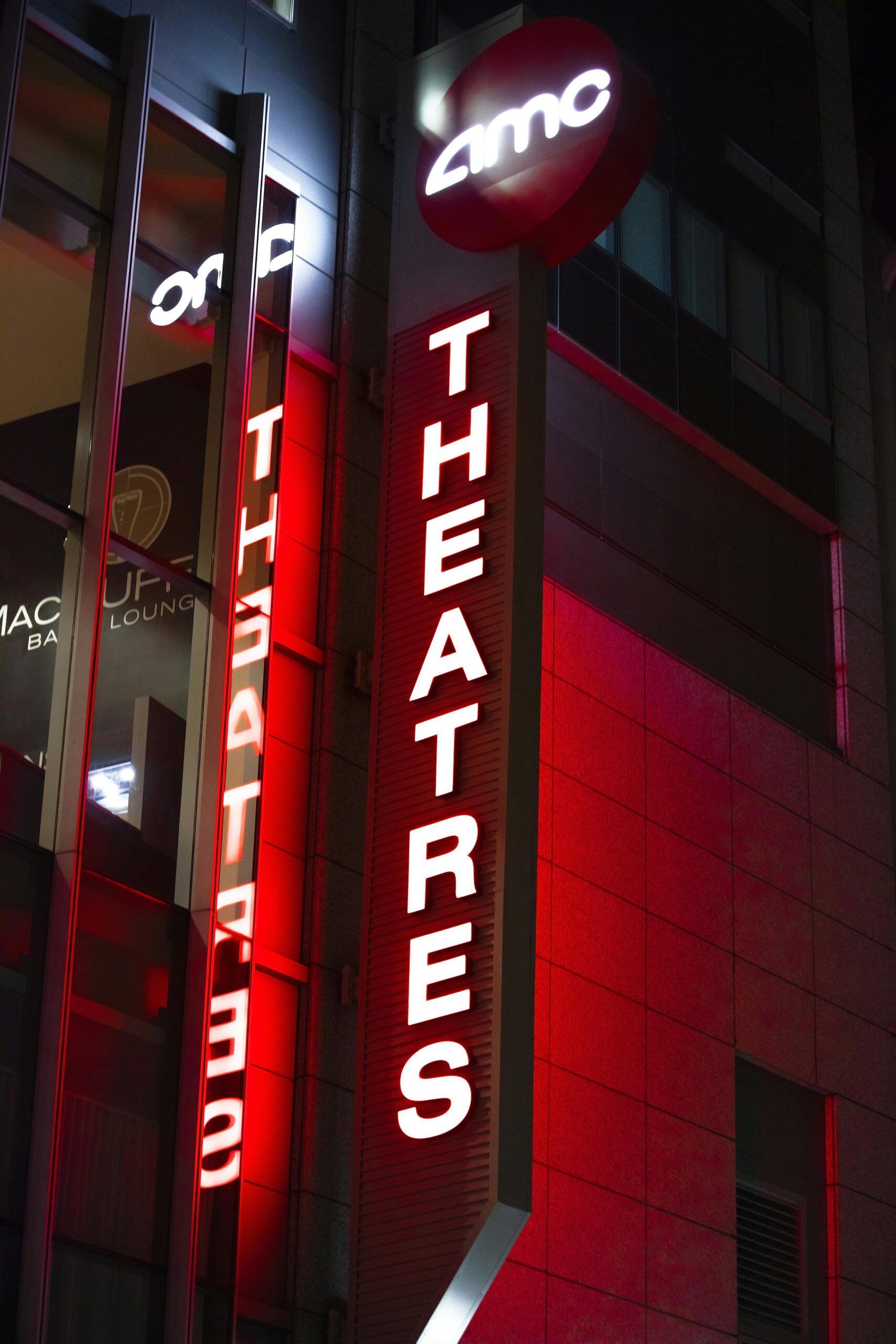 Night view of a neon AMC Theatres sign illuminating the streets of Boston.