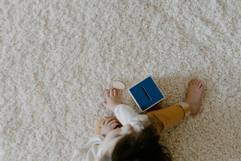 A young child sits on a carpet, engaging with wooden toys and a blue box, captured in a cozy indoor setting. After carpet cleaning in Kent by B Clean Cleaning