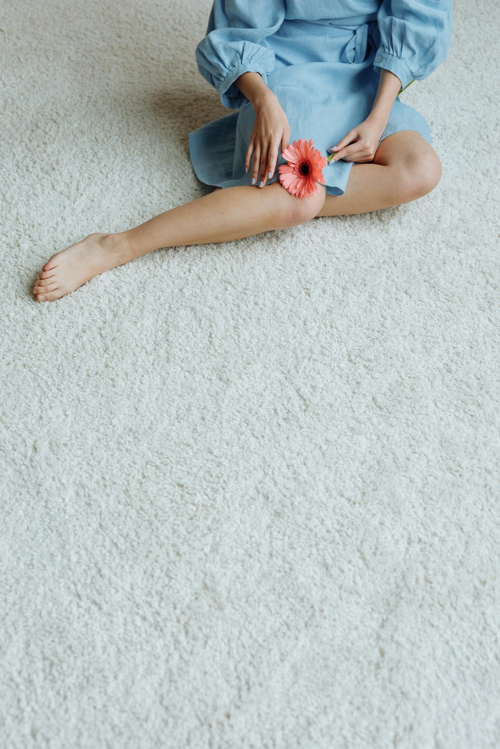Stylish woman in blue dress sitting on a carpet holding a pink flower.